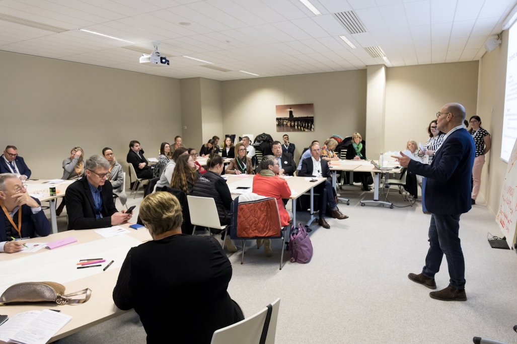 Photo d'un atelier pratique. Des personnes sont assises et écoutent un des animateurs qui a la parole.