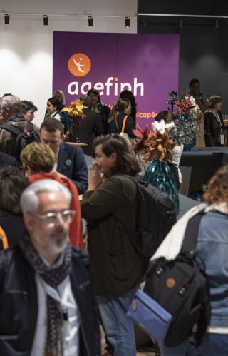 Photo de participants à l'URRH 2022, dans le forum exposant Inspiraction et au fond une affiche du logo Agefiph sur fond violet