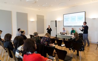 URRH 2023 - Photo des participants de l'atelier LSF. Au premier plan, le public, assis sur des chaises. Dans le fond, une personne debout (à droite) prend la parole avec un micro, 2 personnes au centre, assises, écoutent cette personne et une 4ème, à gauche et debout, traduit en langue des signes française (LSF).