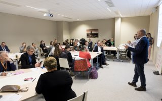 Photo d'un atelier pratique. Des personnes sont assises et écoutent un des animateurs qui a la parole.