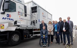 Photo prise de huit personnes debout à droite du camion aménagé pour des personnes en situation de handicap. Sur le camion, apparaissent les logos d'Opco Mobilités, Aftral et Agefiph.