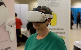 Photo d'une participante qui test un casque de réalité virtuelle, dans l'espace exposant. Sur le stand de Bbird.