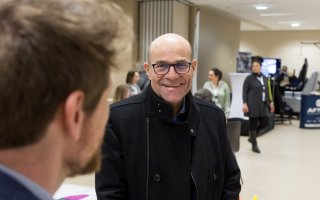 Photo de deux personnes conversant dans l'espace exposant. La personne qui fait face à la caméra arbore un grand sourire.