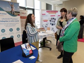 Espace exposant, Pro Adapt. 2 personnes posent des questions à une exposante, au premier plan. En arrière plan apparaissent les stands d'Atomota et de Kunto.