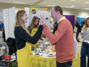 Photo d'un exposant, sur le forum : Kignon. 2 personnes se sourient et font un check de la main, l'une d'entre elle porte le tablier de la biscuiterie Kignon.