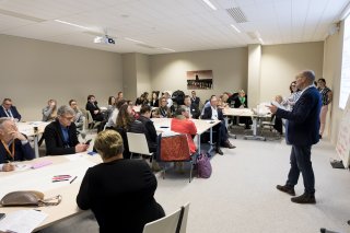 Photo d'un atelier pratique. Des personnes sont assises et écoutent un des animateurs qui a la parole.