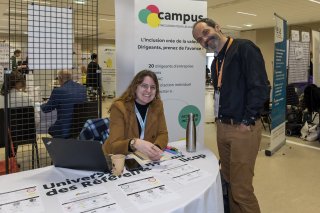 Photo du stand du Campus de l'inclusion. 2 personnes prennent la pose et sourient à la caméra.
