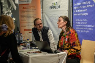 Deux exposants du stand France Travail et Chéops (Cap emploi), discutent avec des personnes